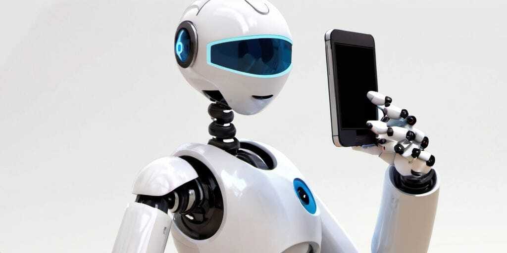 Robot humanoide futurista de color blanco con detalles en negro y azul, sosteniendo un teléfono inteligente con una mano robótica. El robot tiene un diseño elegante, con visor azul y líneas modernas, representando tecnología avanzada y conectividad.
