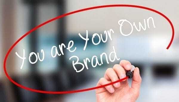 La imagen muestra una mano sosteniendo un marcador mientras escribe la frase "You are your own brand" (Eres tu propia marca) en una superficie transparente o en el aire, con la frase encerrada dentro de un círculo rojo. El fondo está ligeramente desenfocado, lo que resalta el mensaje principal sobre la importancia de la marca personal.